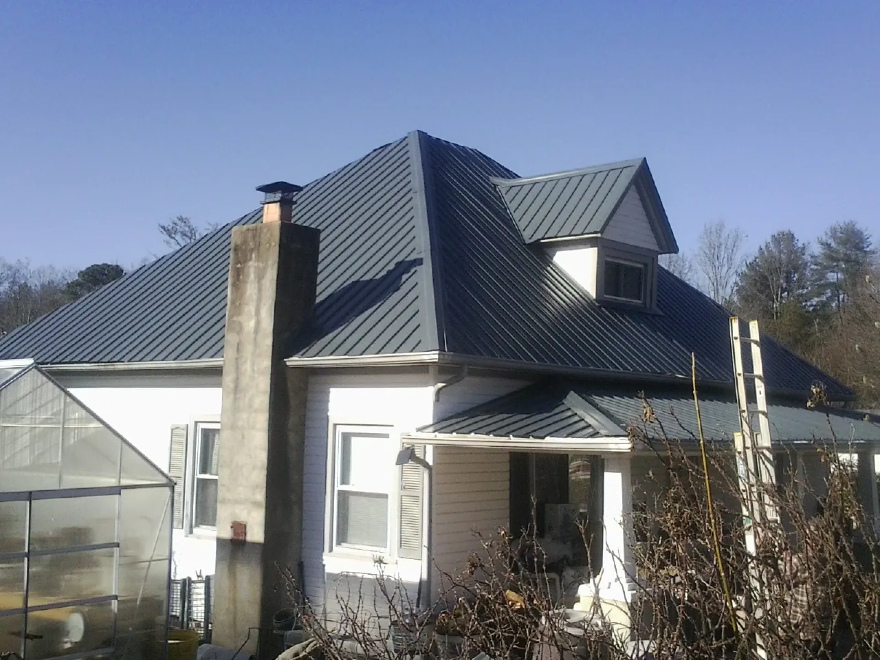 Dark blue standing seam metal roof on a white farmhouse with dormer — Slate & Tile Roof Repair by Roofing Brothers in Rifle