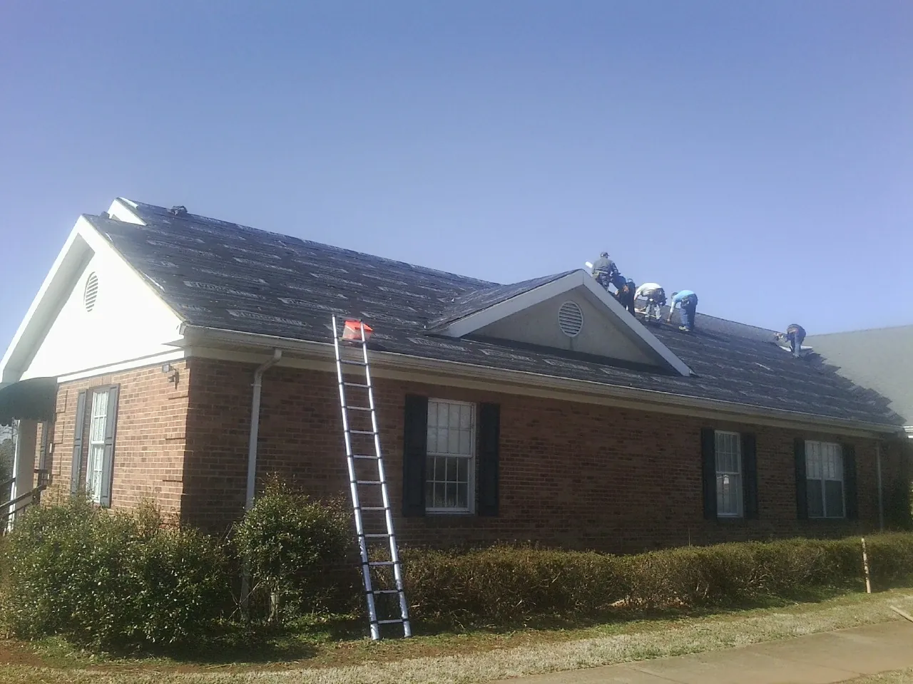 Crew tearing shingles off a brick ranch roof with a ladder set — Emergency Roof Repair work by our crew in Rifle