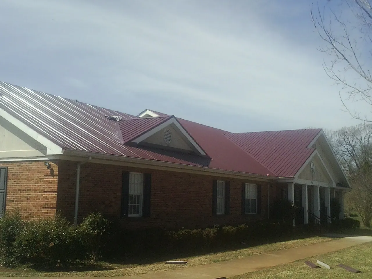 Red metal roof with gabled entries on a long brick building, from a Hail Damage Roof Repair job in Rifle
