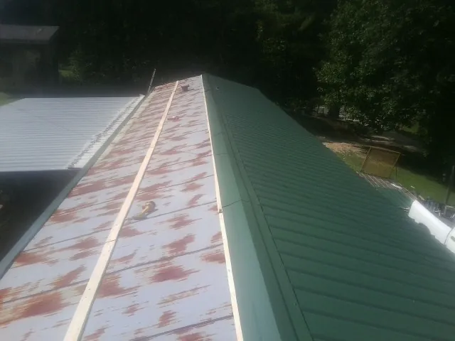 Old rusted panels beside newly installed green metal roofing — Wind Damage Roof Repair by Roofing Brothers in Rifle