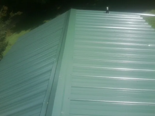 New green metal panels meeting at the ridge of a roof — Flat Roof Repair work by our crew in Rifle