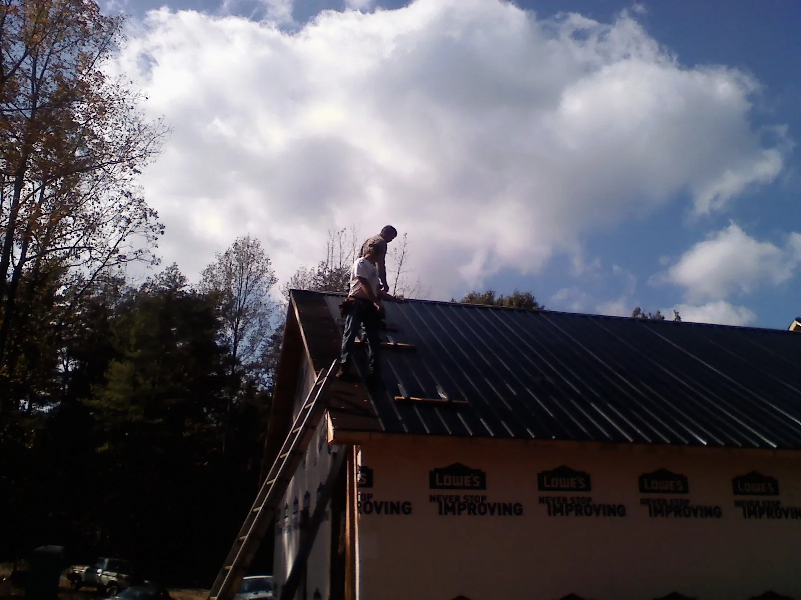 Roofer fastening dark metal panels high against a cloudy sky, from a Roof Inspection job in Rifle
